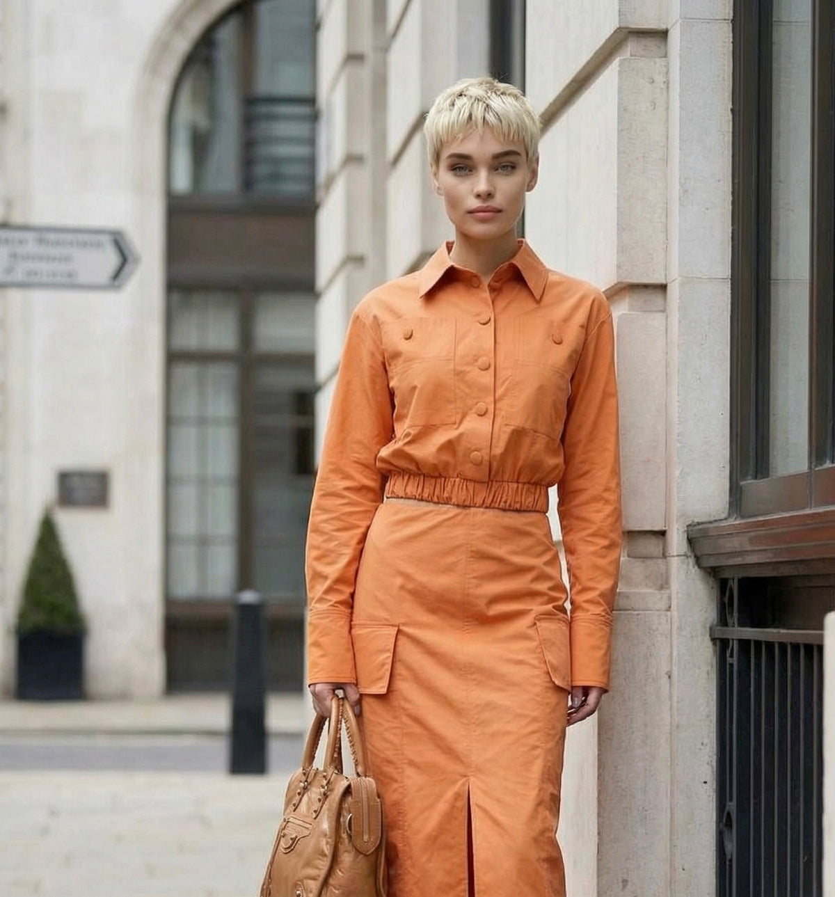Woman in an copper tan dress by Resident Stranger, standing on a city street.