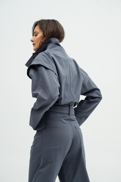 A model shown from the back wearing a Aisuru jacket in stone blue color  and matching Rei high-waisted trousers against a light gray studio background.