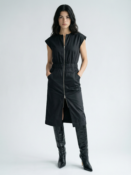 Woman wearing a black sleeveless dress with a zipper and black knee-high boots on a white background