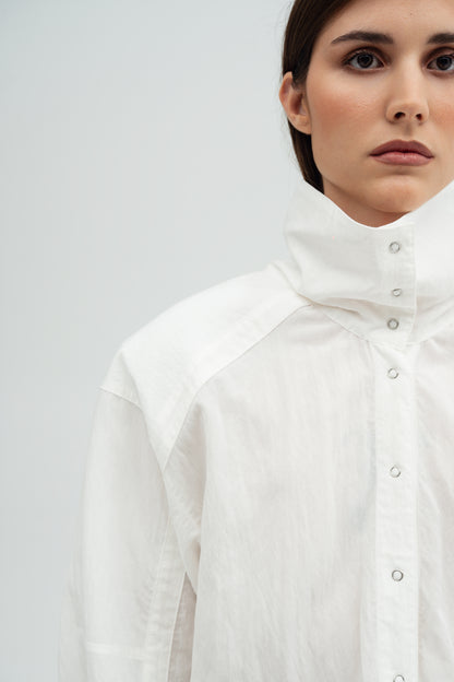 A close-up of a model wearing a white Nume high-neck button-up shirt Resident Stranger  with textured fabric and silver snaps.
