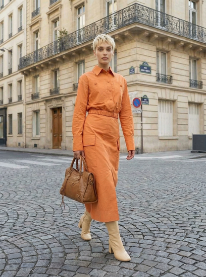 Woman in an orange outfit walking on a cobblestone street in an urban setting